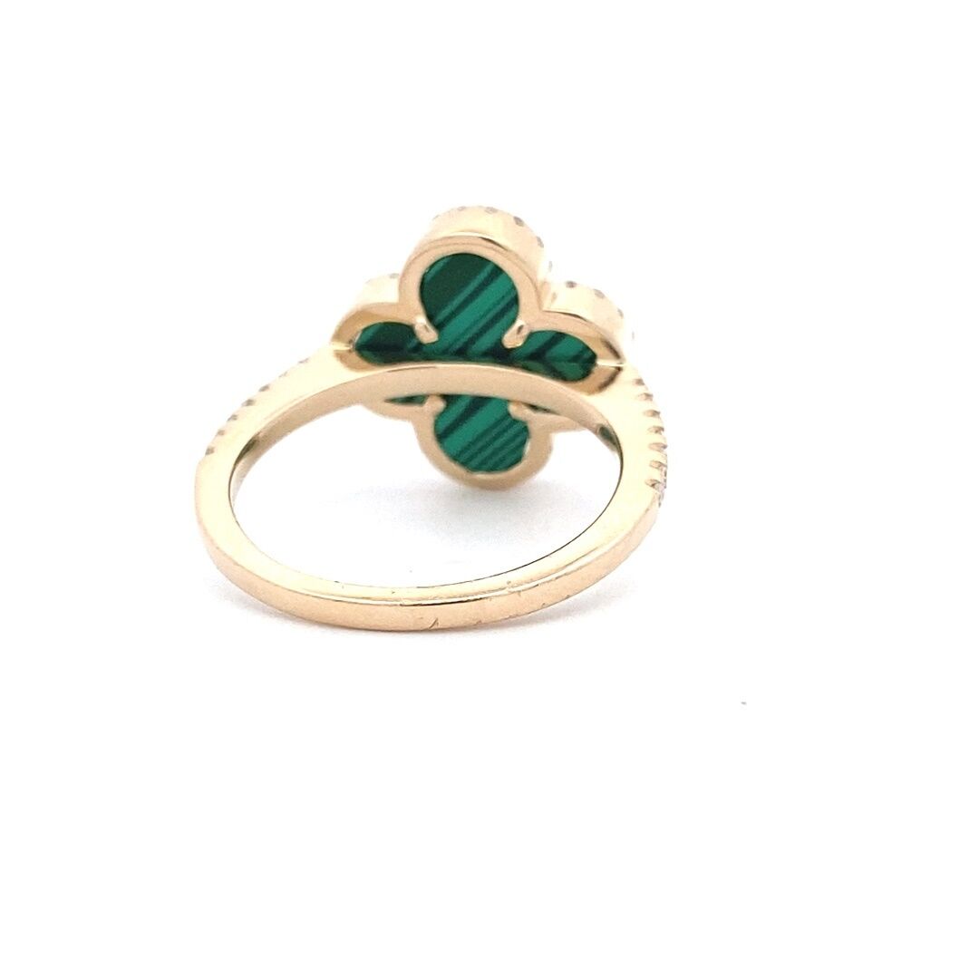 A yellow gold clover ring set with a flat piece of malachite and diamond halo