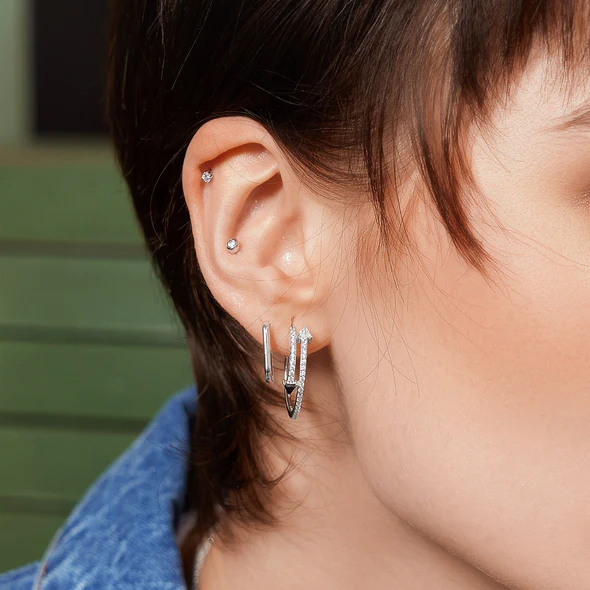 Sterling Silver Large Oval Huggie Hoop Earrings on a model with short brown hair stacked with other hoop and stud earrings