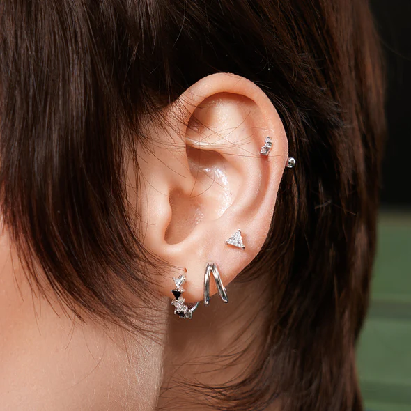 A model wearing Sterling Silver Double Huggie Hoop Earrings by Ania Haie stacked with other stud and hoop earrings by Ania Haie